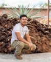 Man crouching near agave plants ready for mezcal production outdoors.
